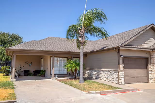 Single-story senior living facility exterior with driveway, palm tree, and attached garage.