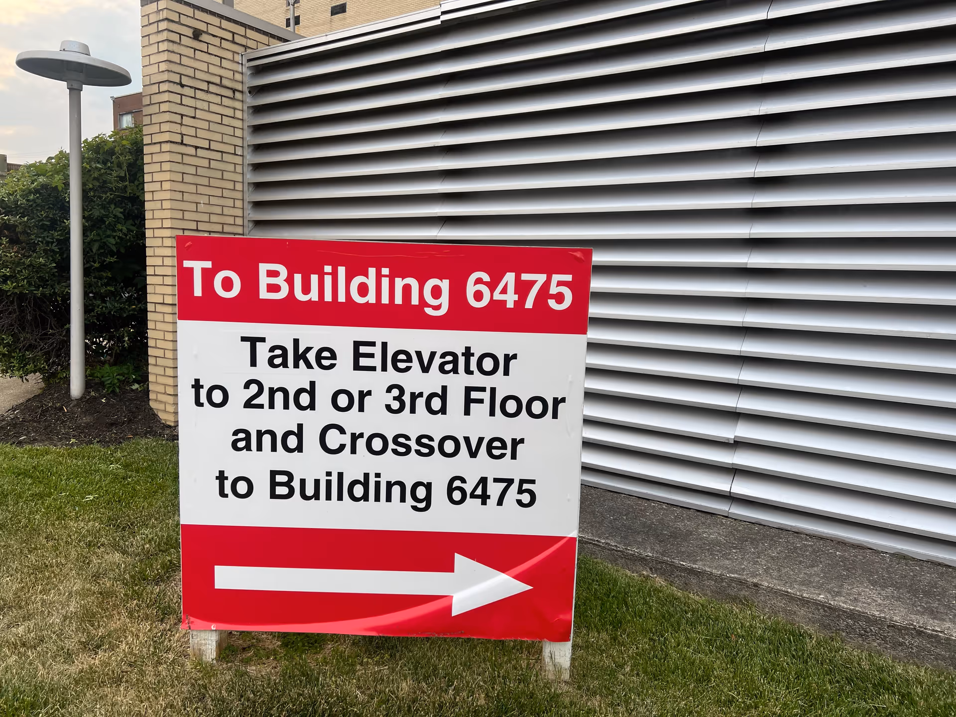 Red and white directional sign outside building with elevator instructions.