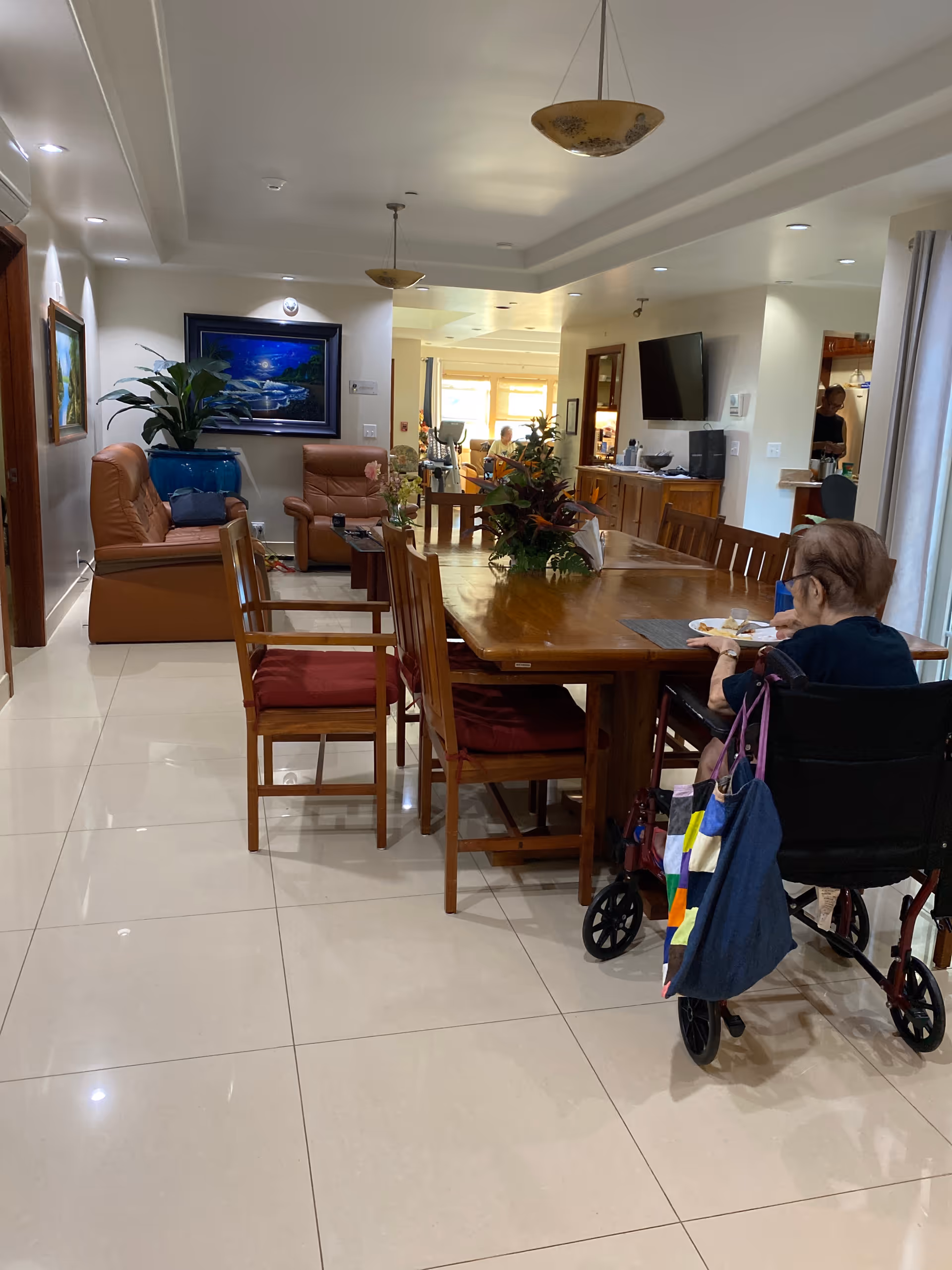 A well-lit senior living dining area with a wooden table, chairs, and residents.