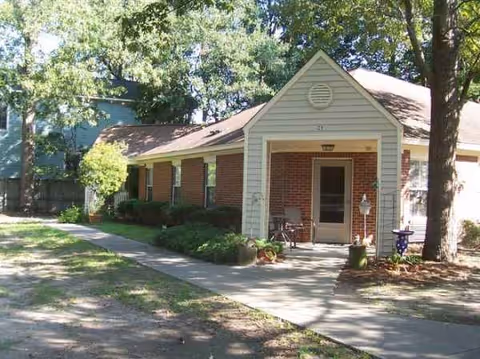 Exterior view of a brick senior living facility with a small front porch and surrounding trees.