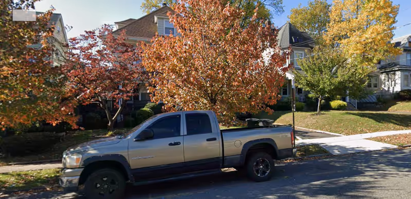 Silver pickup truck parked on a residential street with autumn trees and houses.