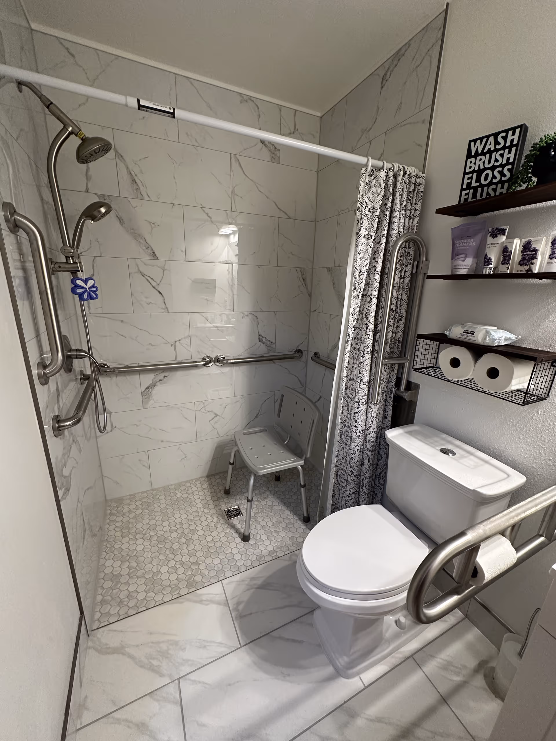 Accessible bathroom with a walk-in shower, shower chair, grab bars, and toilet.