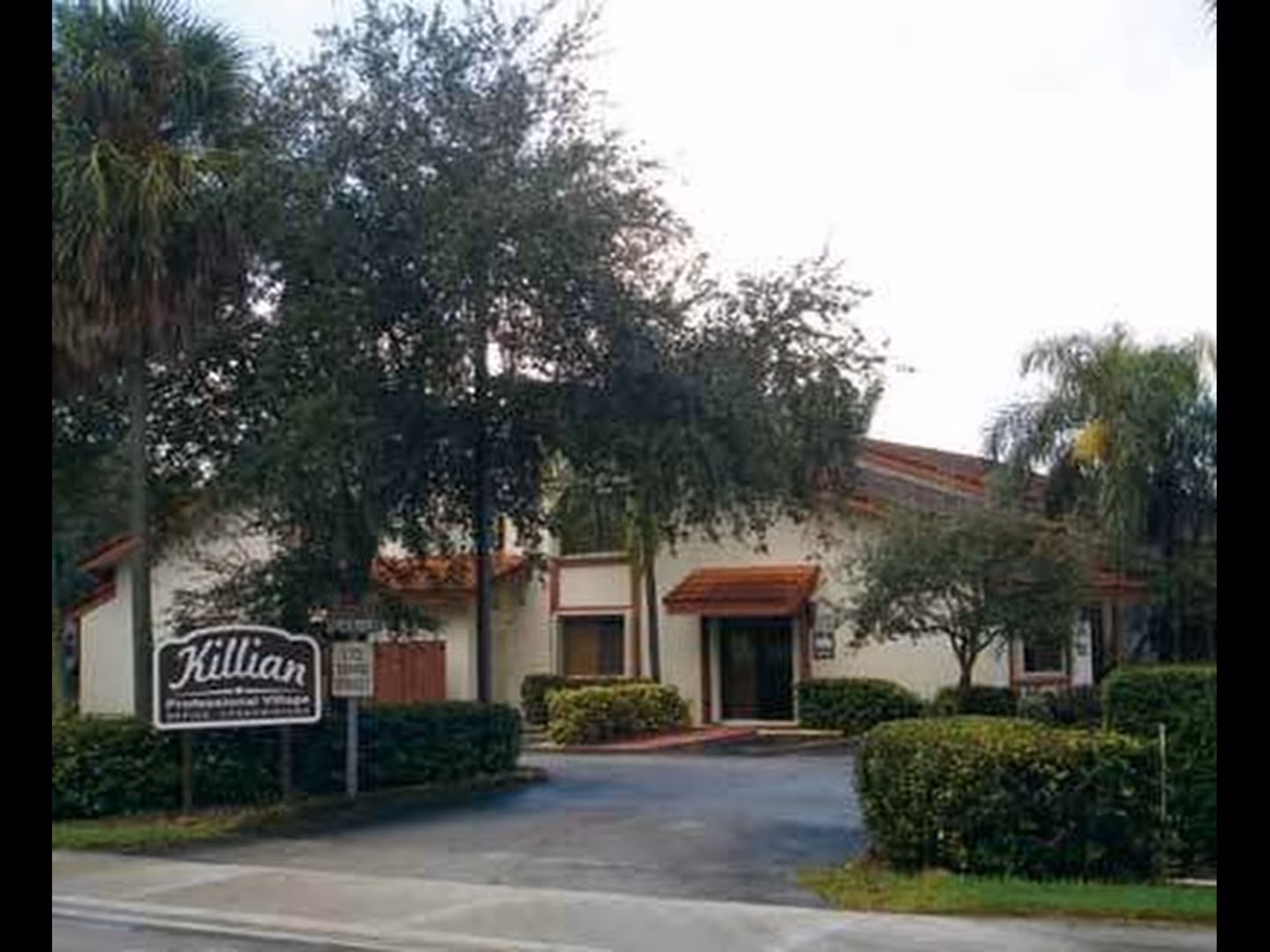 Front view of a single-story senior living building with a driveway and landscaped shrubs.