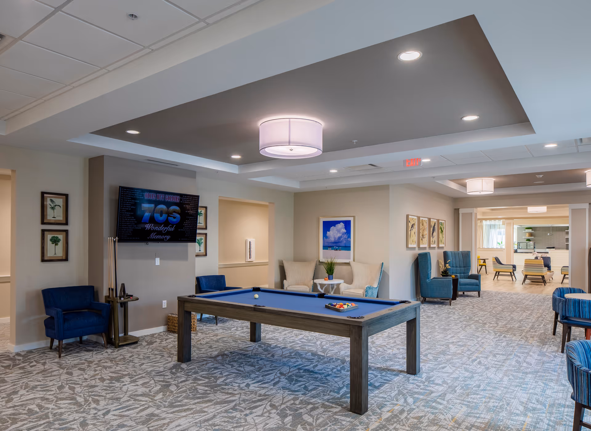 Spacious senior living lounge with a pool table, blue seating, and wall art.