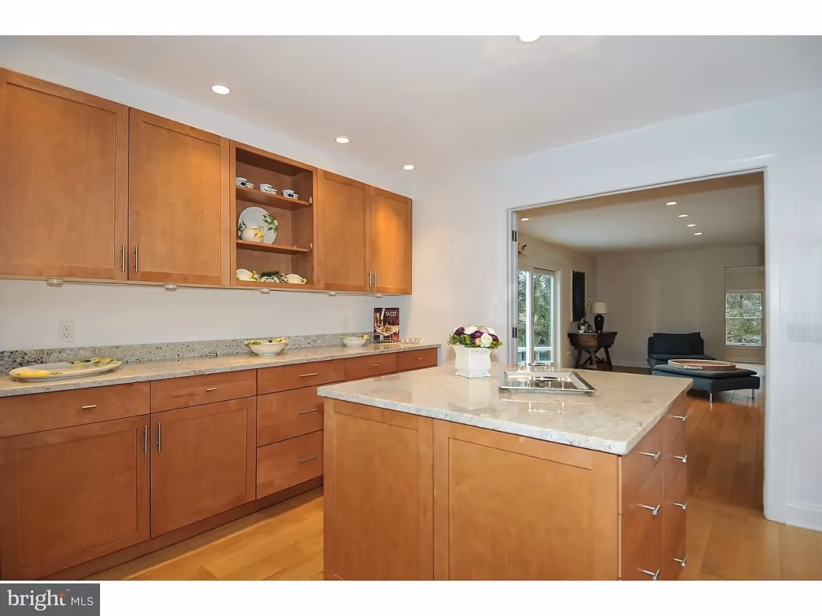 Bright modern kitchen with wooden cabinets, granite countertops, and a central island opening into a living area.