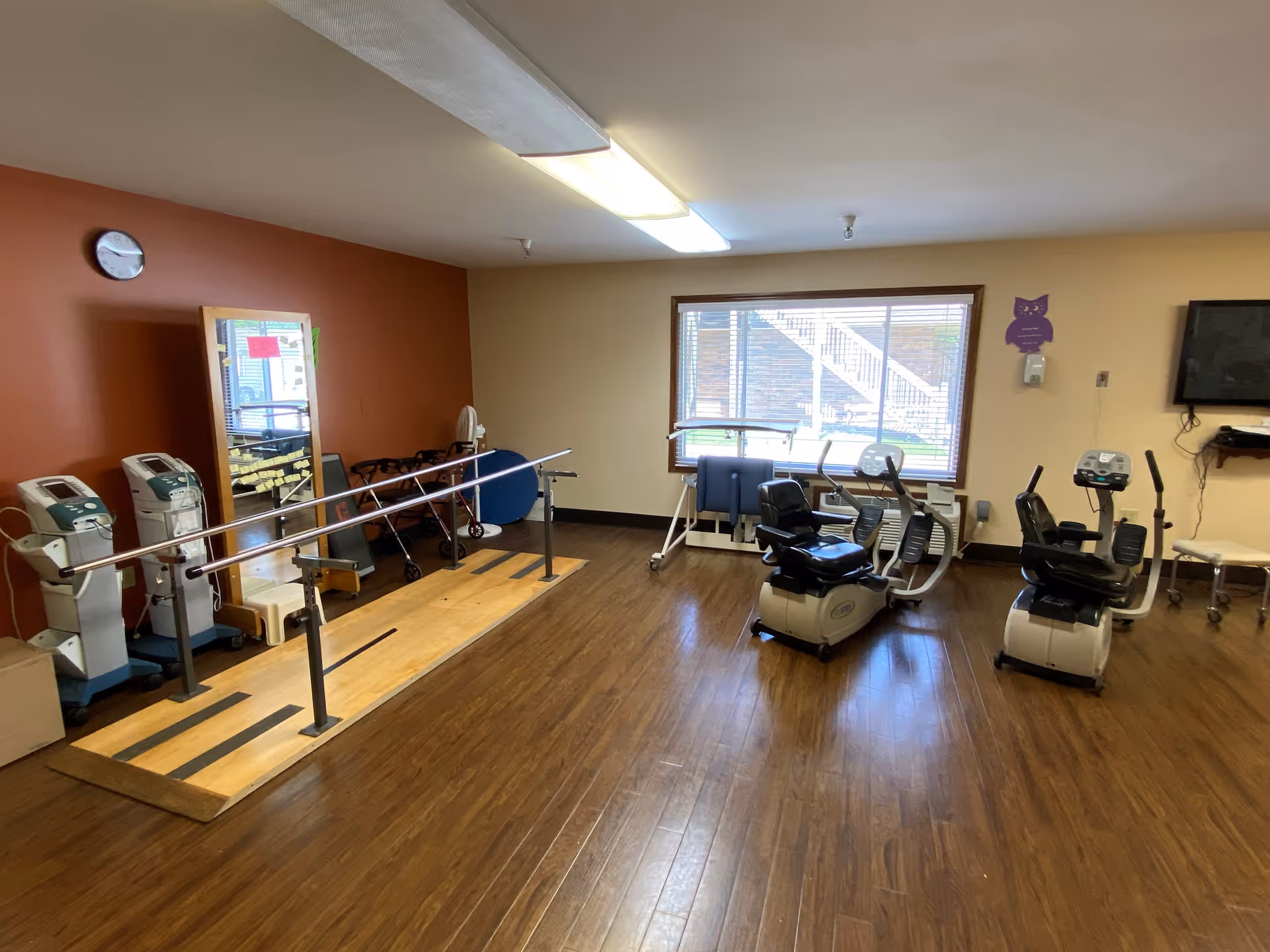 Indoor rehabilitation gym with parallel bars, exercise bikes, and wooden flooring.