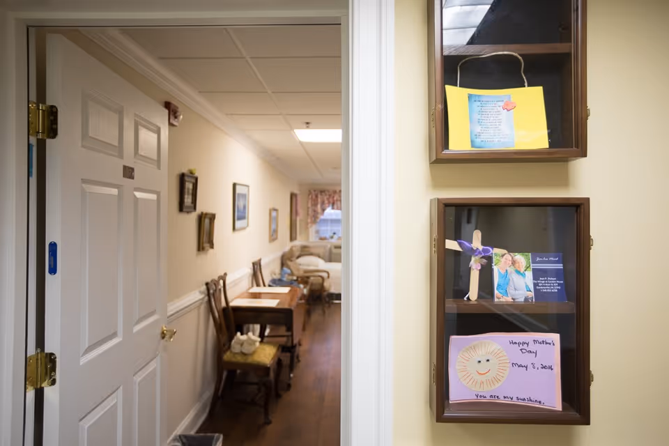 Interior hallway view into a sitting area with chairs and tables, and two glass-front wall display cases holding cards on the right.