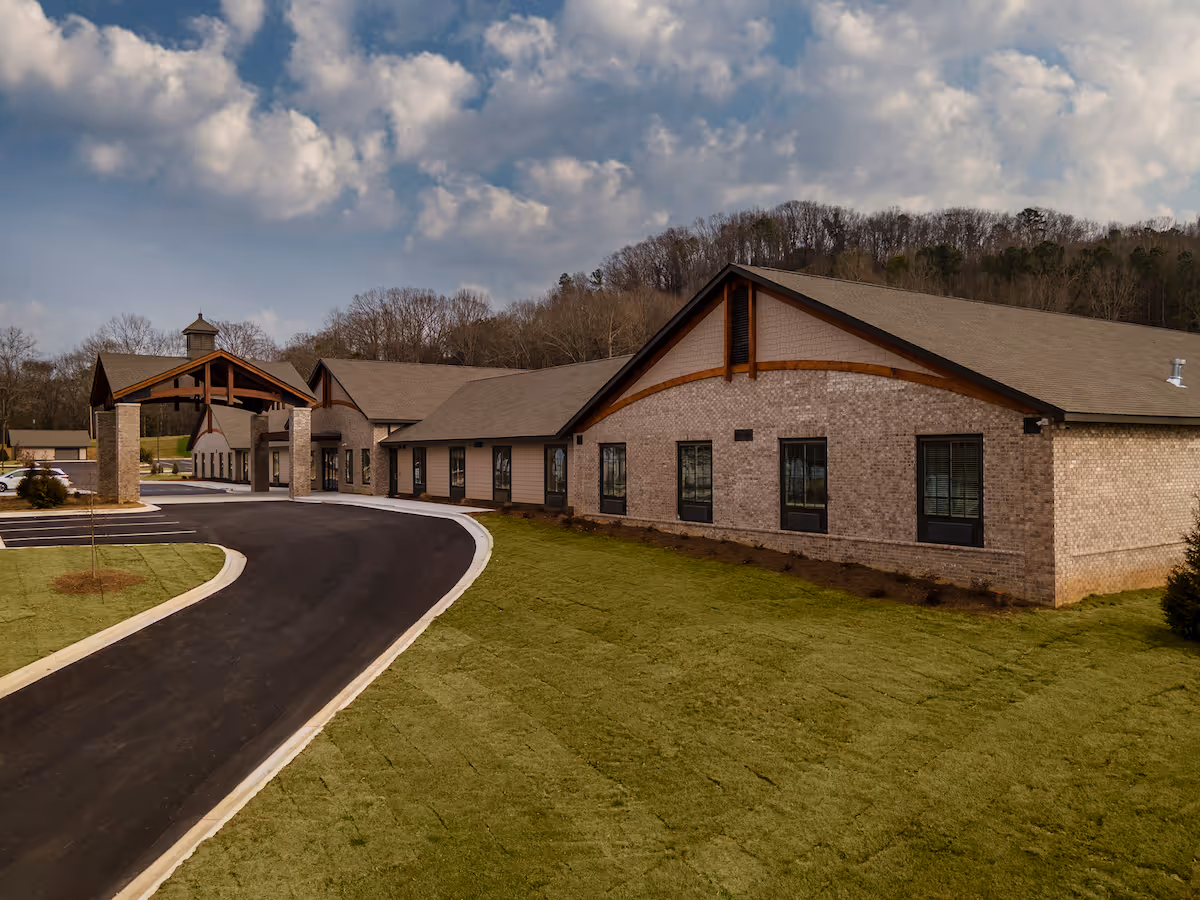 Brick senior living building with curved driveway and covered entrance under a cloudy sky.