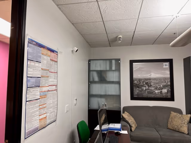 Office-like room with desk, chair, couch, and framed cityscape.