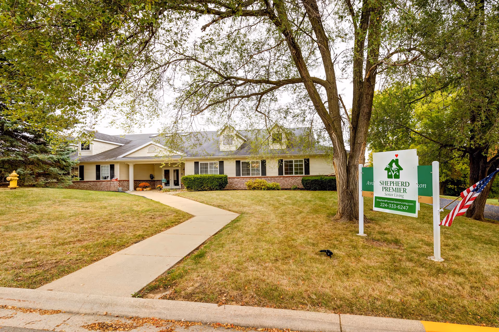Exterior view of Shepherd Premier Senior Living with sign, walkway, and trees.