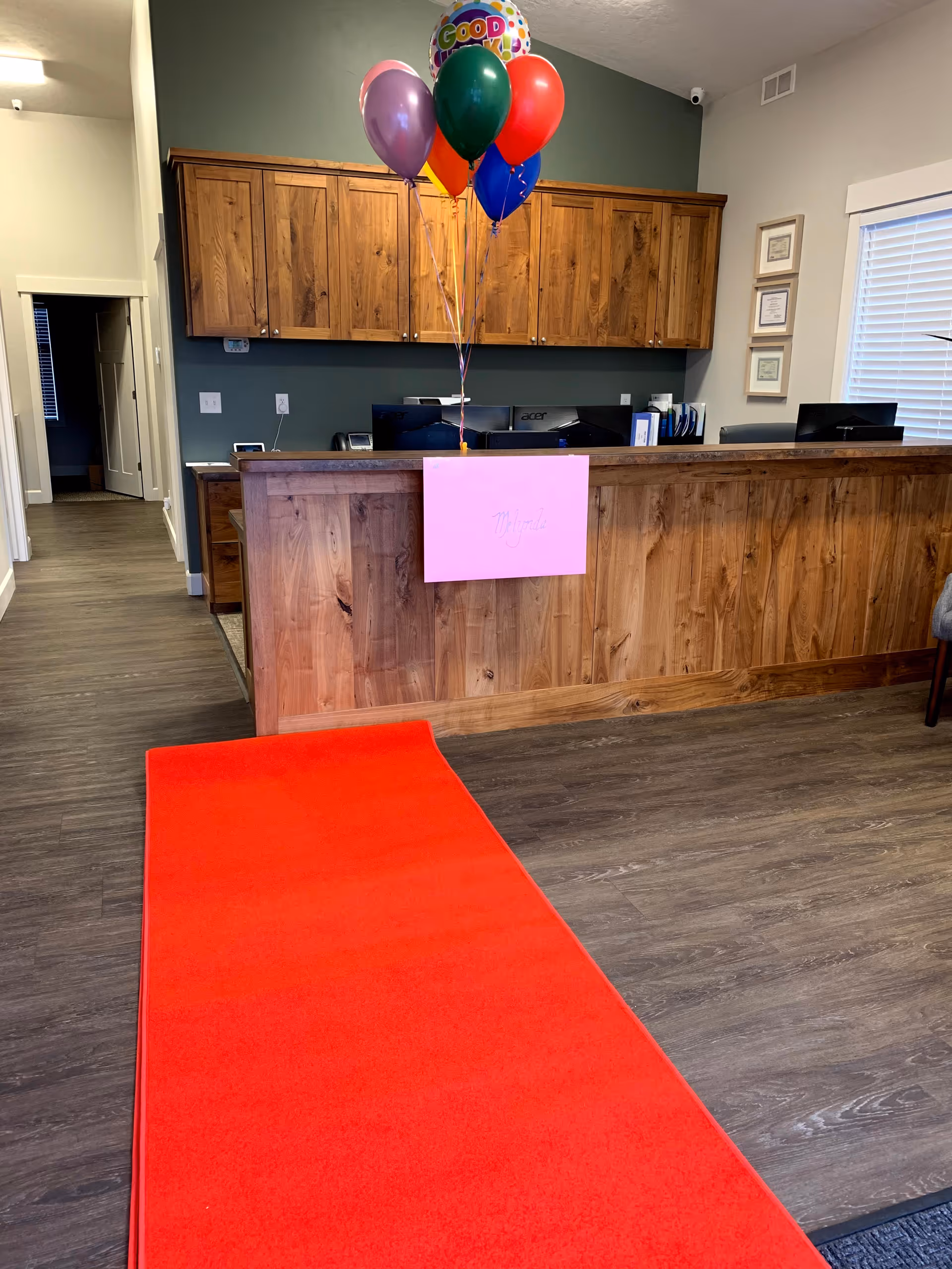 Reception desk with balloons and a pink sign in a wood-paneled lobby.
