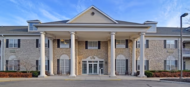 Front entrance of a multi-story senior living facility with large white columns, stone façade, and a covered portico.