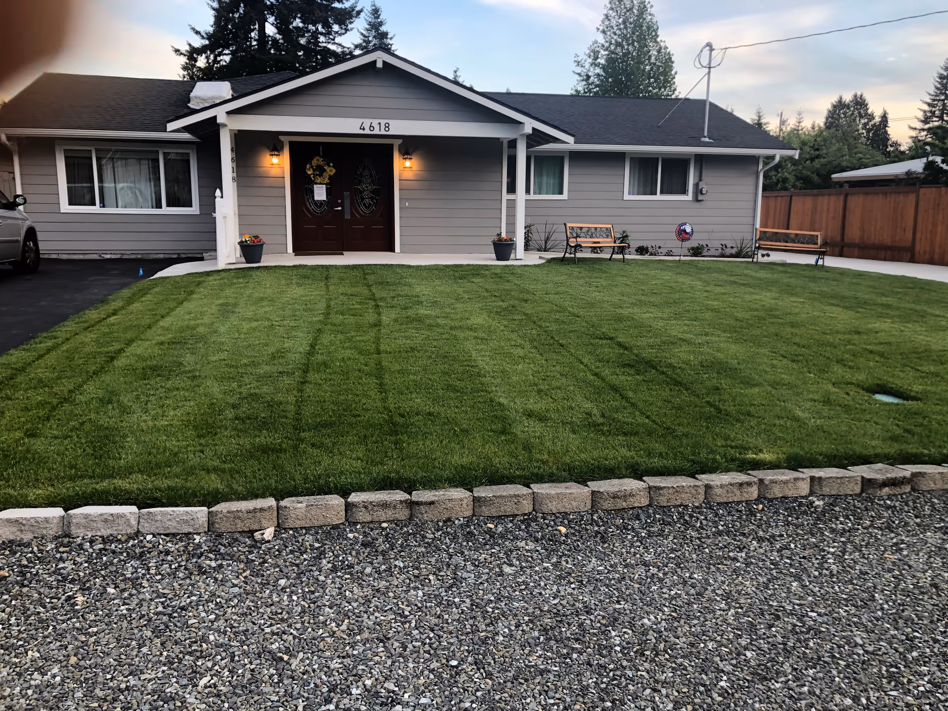 A single-story gray adult family home with a manicured front lawn and benches.