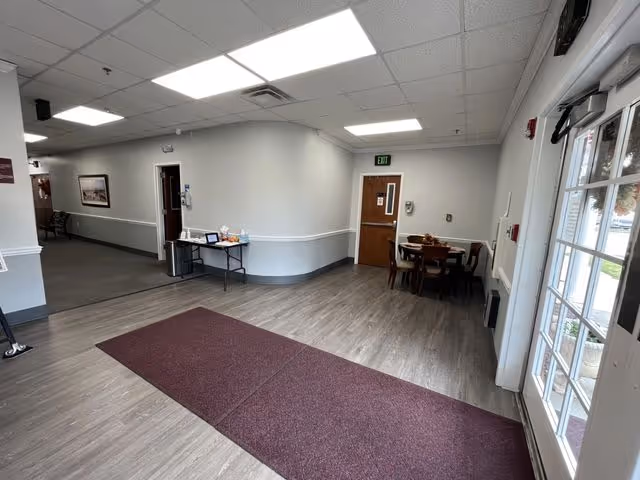Empty senior living lobby with gray walls, ceiling lights, and a red carpet runner.