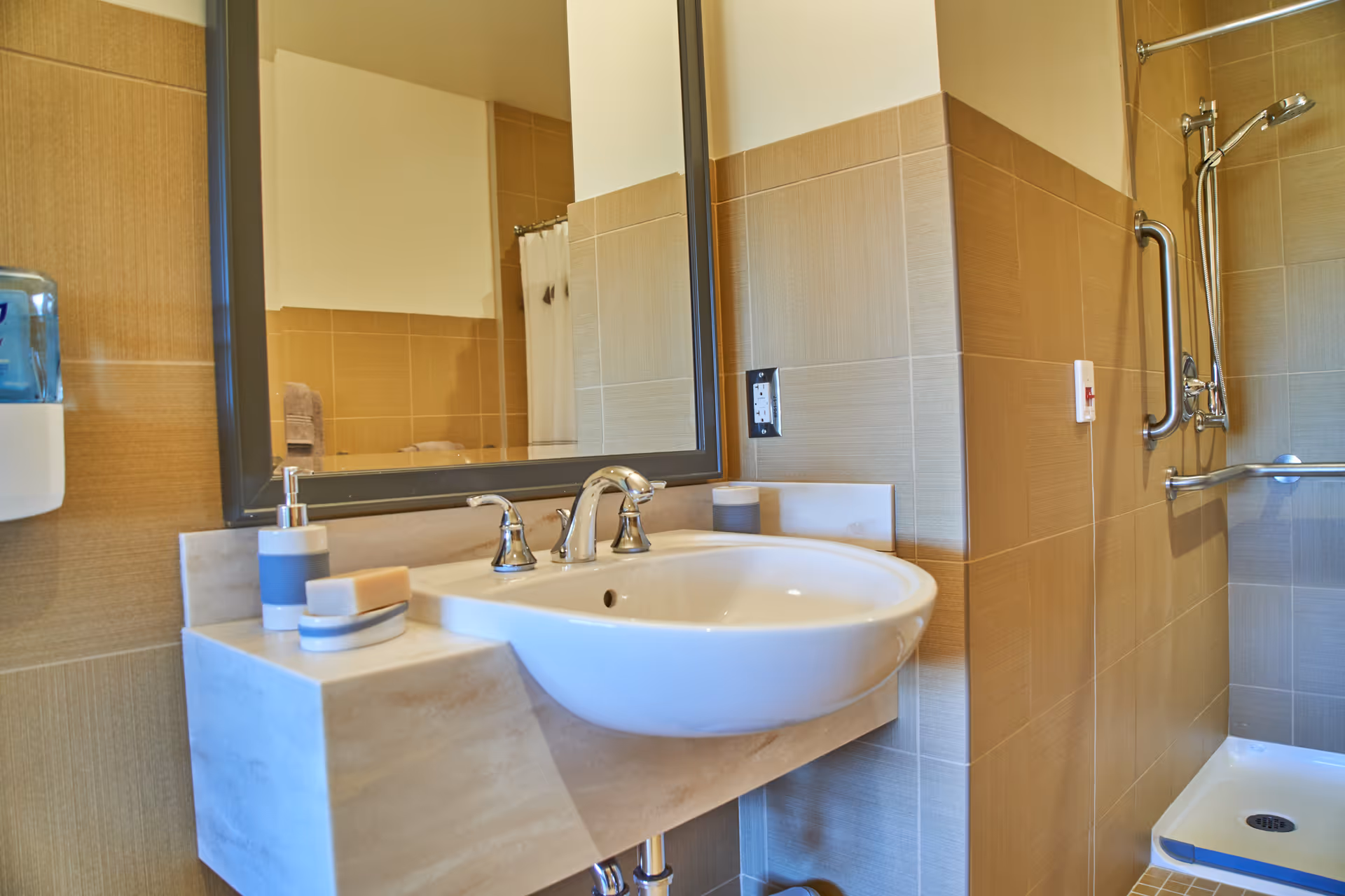 Bathroom with sink, mirror, and shower area featuring grab bars