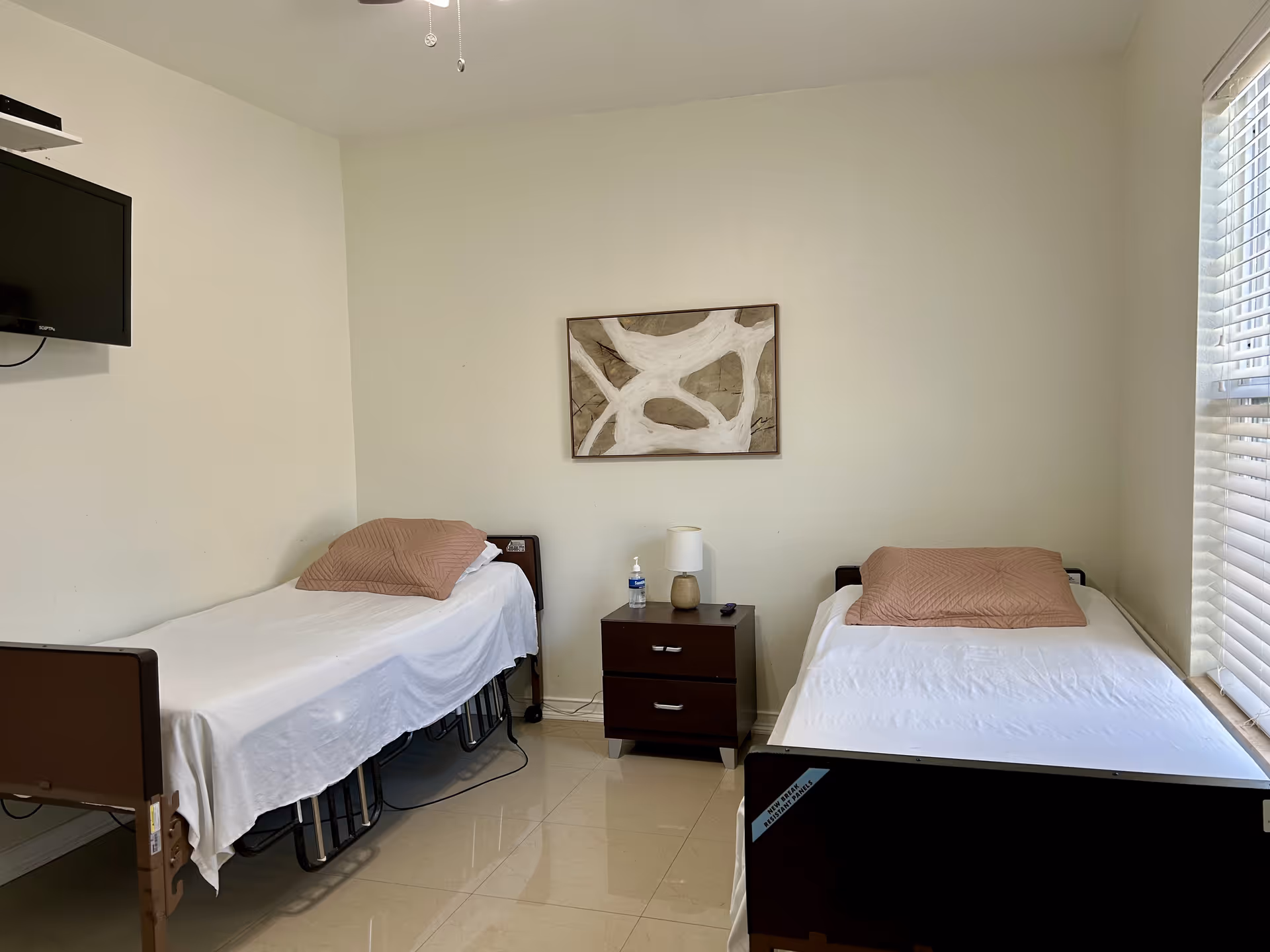 Two single beds with a nightstand, TV, and abstract wall art in a bright room.
