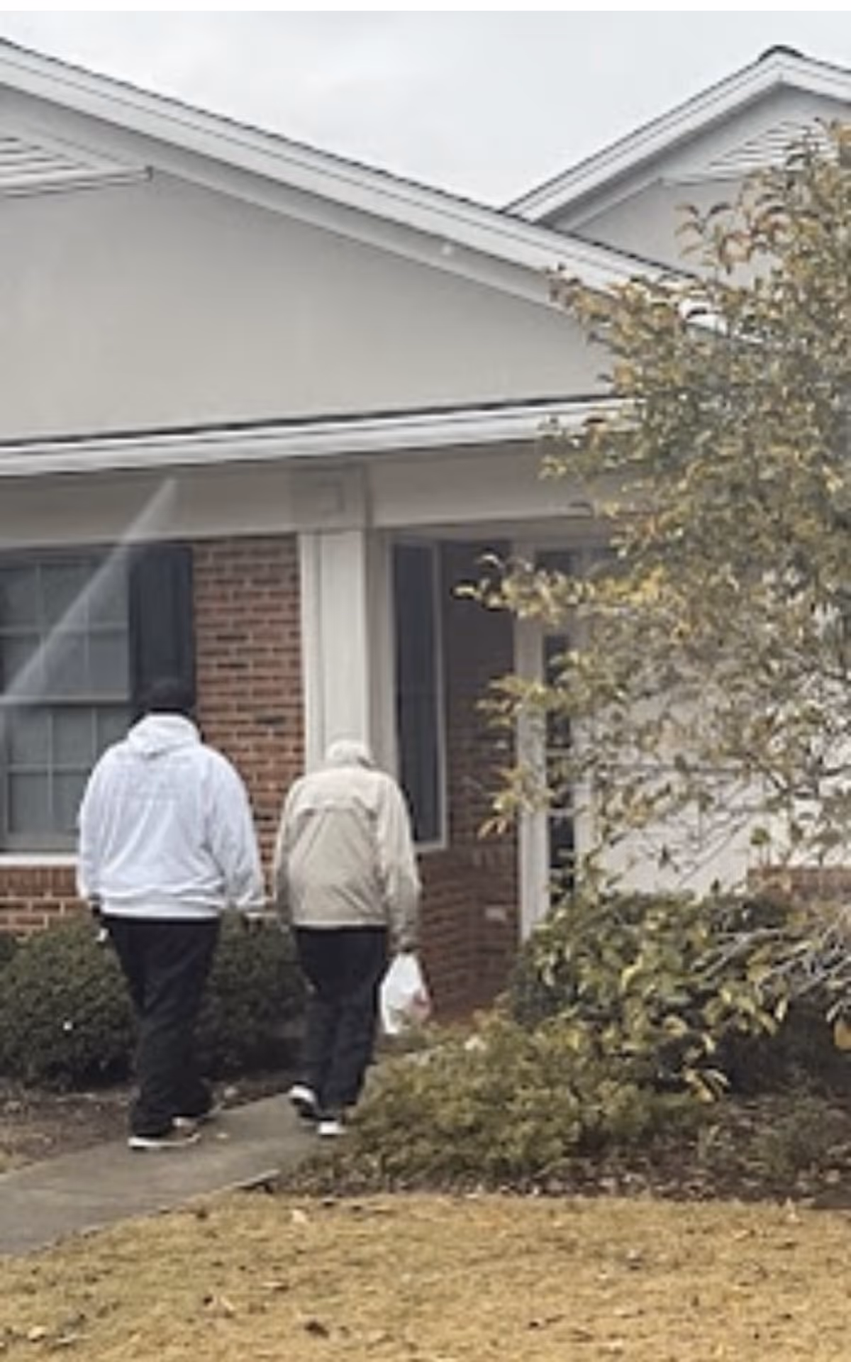 Two elderly residents walk toward the facility entrance on a cloudy day.