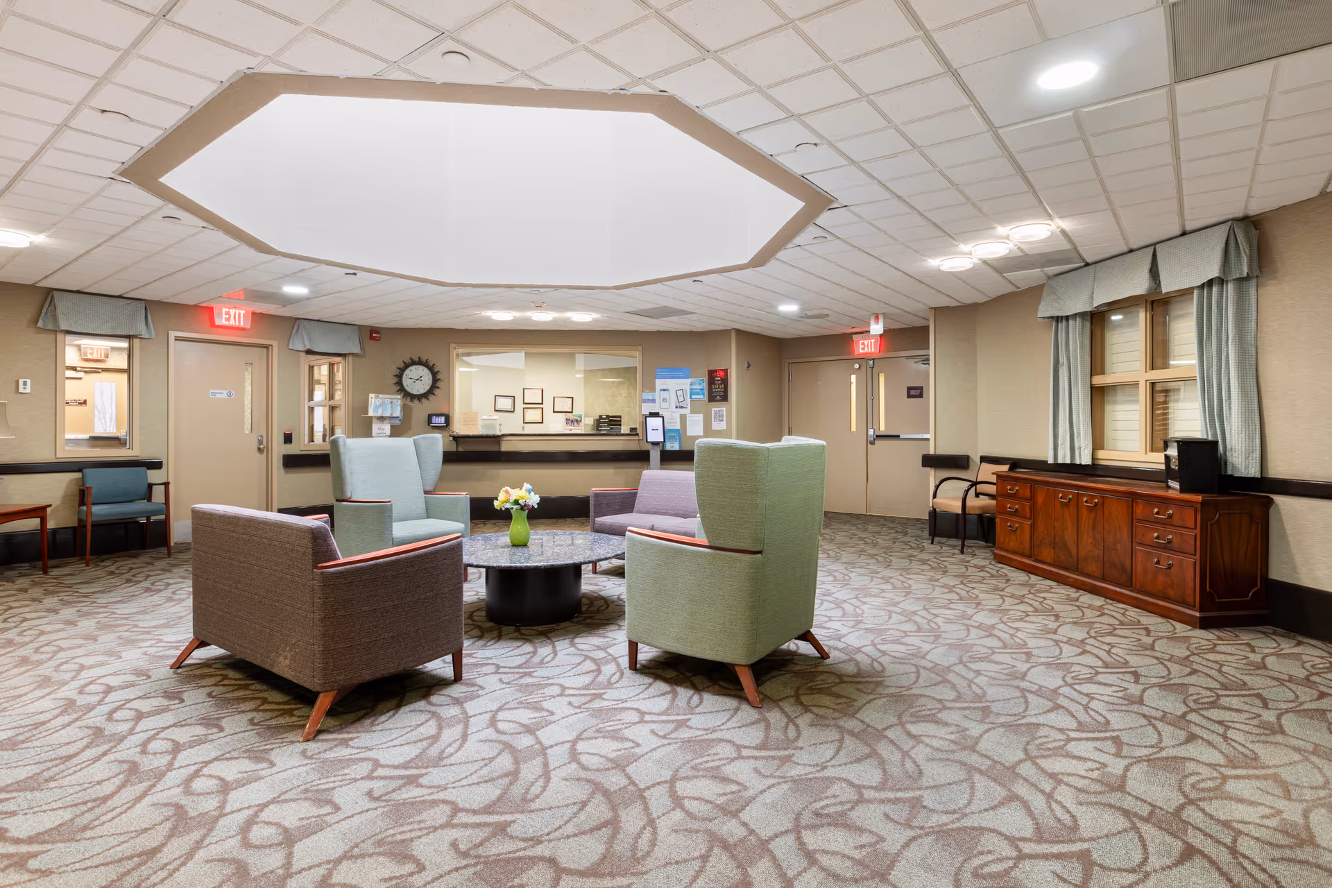 Spacious indoor lounge at a senior care center with circular seating and a reception desk.