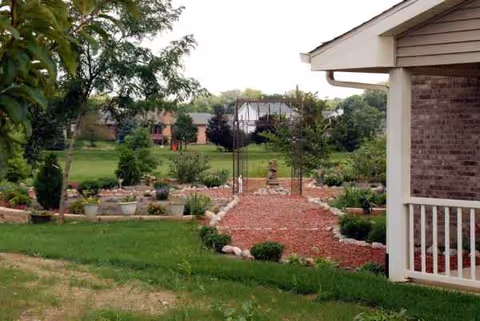 Front yard garden with brick path, potted plants, and a partial porch on the right