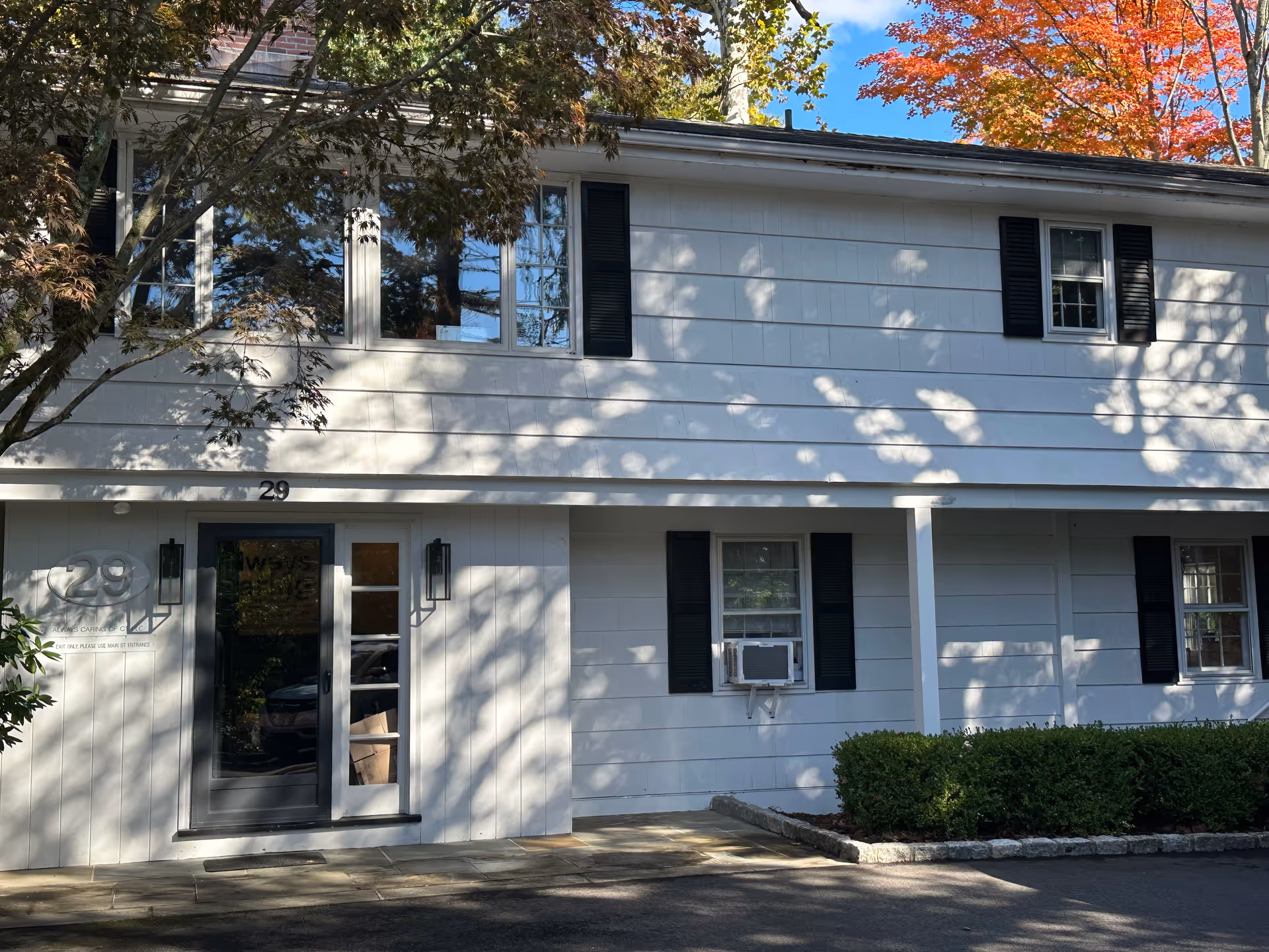 White two-story building with black shutters, shaded entrance, address 29.