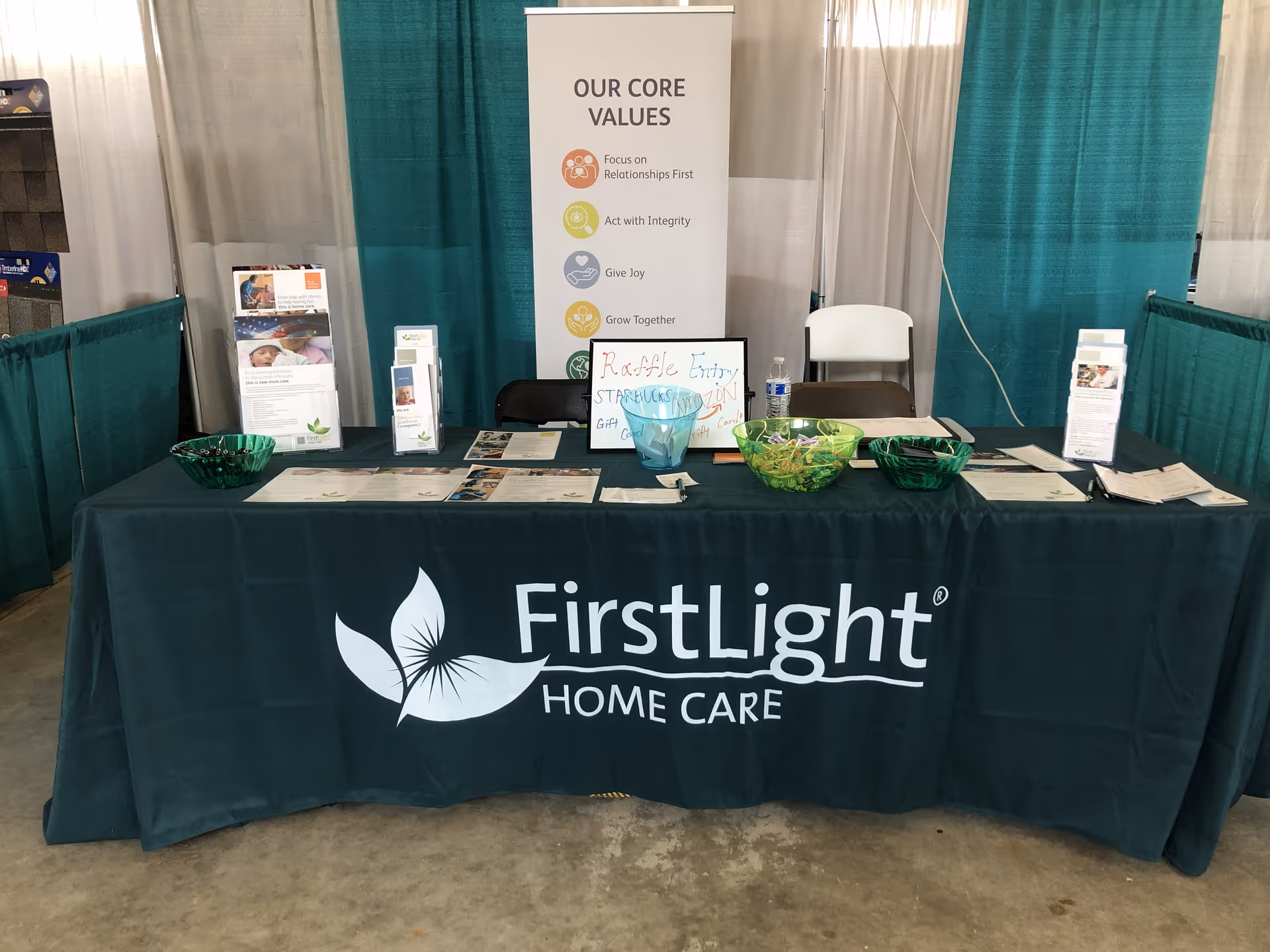 Indoor expo booth with a FirstLight Home Care banner on teal tablecloth.