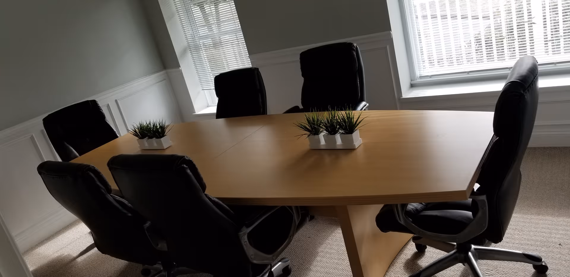 A wooden conference table with six black chairs in a bright windowed room.