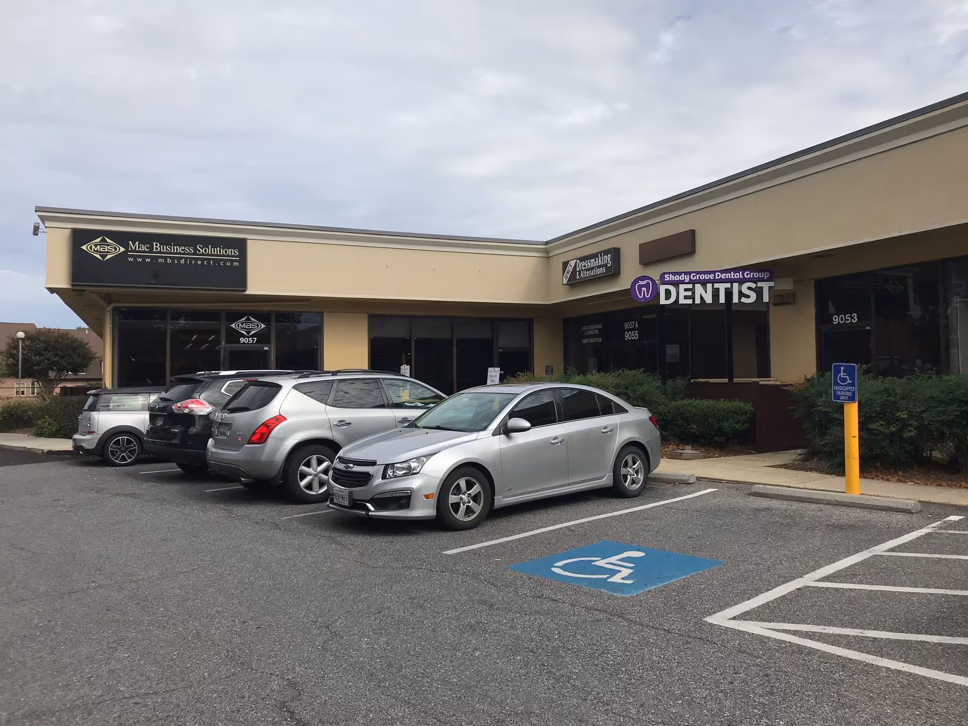 Strip mall storefronts with parked cars in front, including a visible handicap-accessible space.