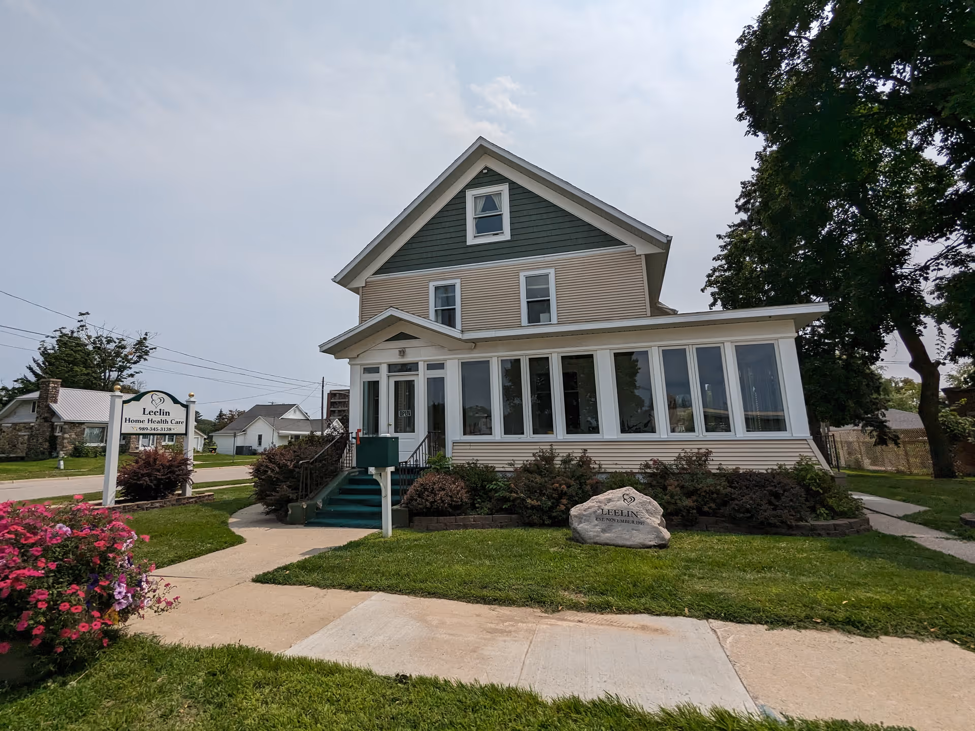 Two-story house-style care facility with a glass-enclosed front porch and manicured landscaping.