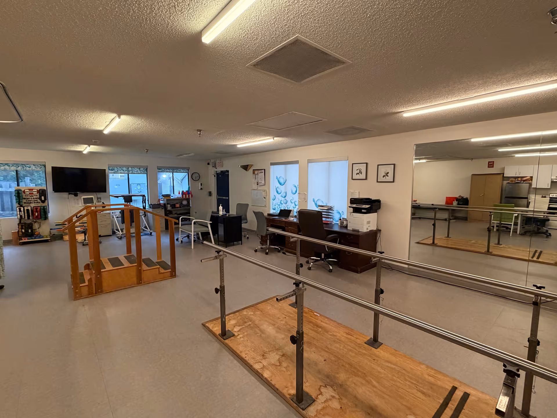 Interior rehabilitation gym at Shamrock Nursing Center with parallel bars and exercise equipment.
