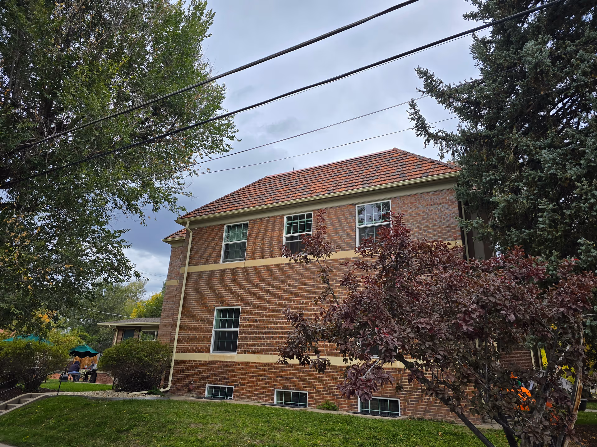 Two-story brick building with a tiled roof surrounded by trees and a grassy lawn.