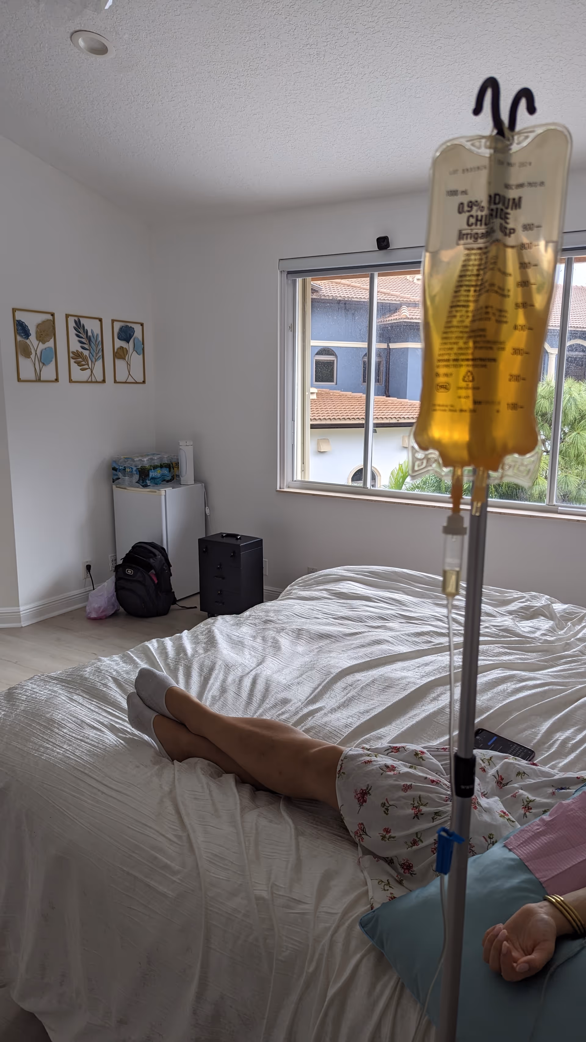 A patient lies in a hospital-style bed in a bright senior living bedroom with an IV.
