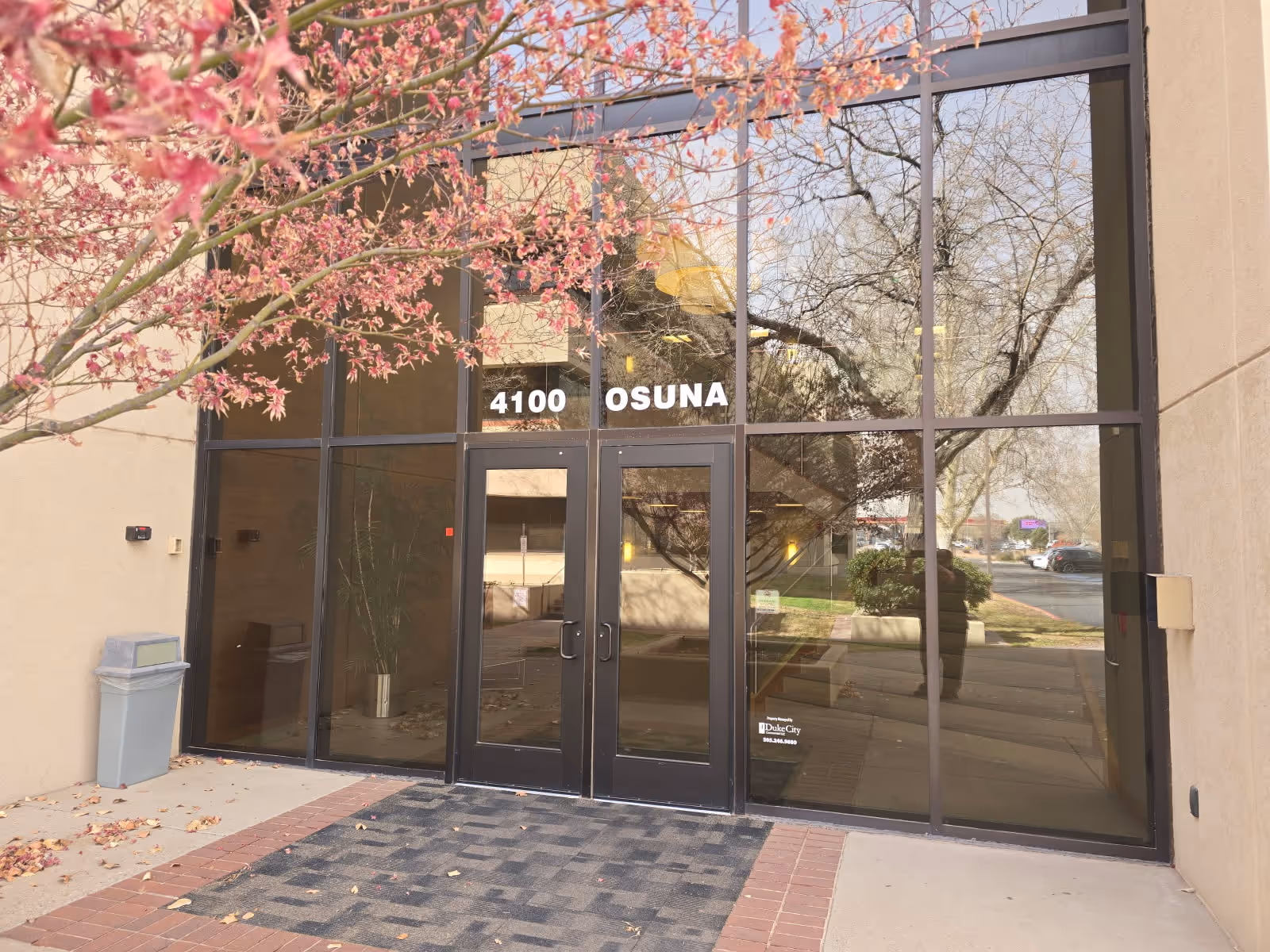 Glass-front entrance with 4100 Osuna address and pink flowering tree nearby.