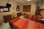Two beds with red quilts in a compact resident bedroom at a senior facility.