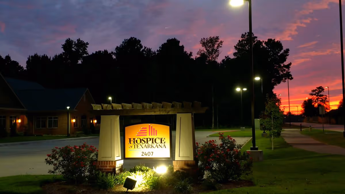 Exterior sign for Hospice of Texarkana with landscaping and a sunset sky.