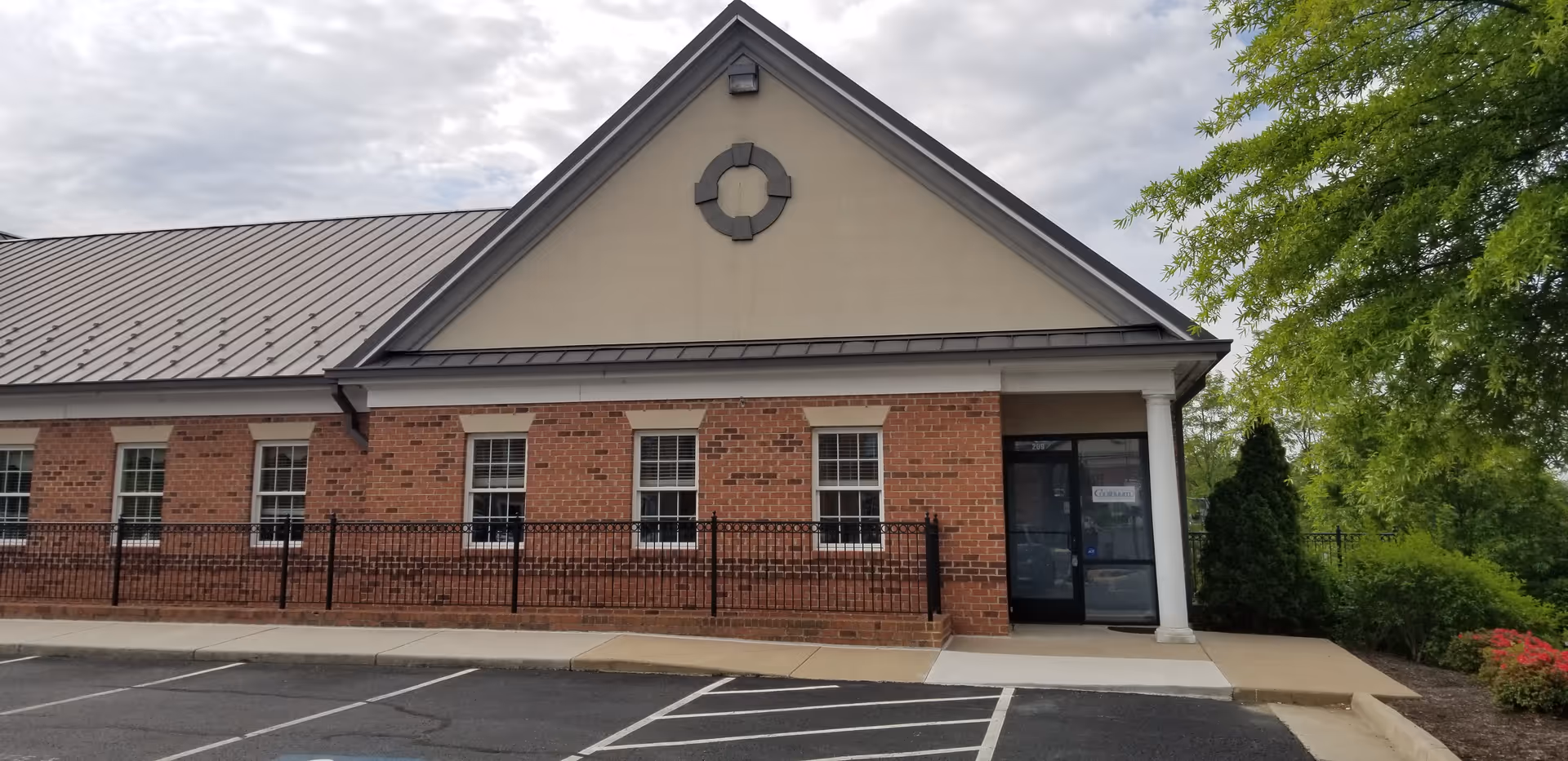 Brick building with a gable roof, circular vent, glass entrance, and a parking lot.