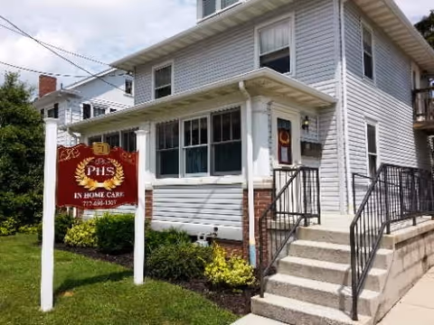 Two-story white senior care facility exterior with a front sign and metal stairs.
