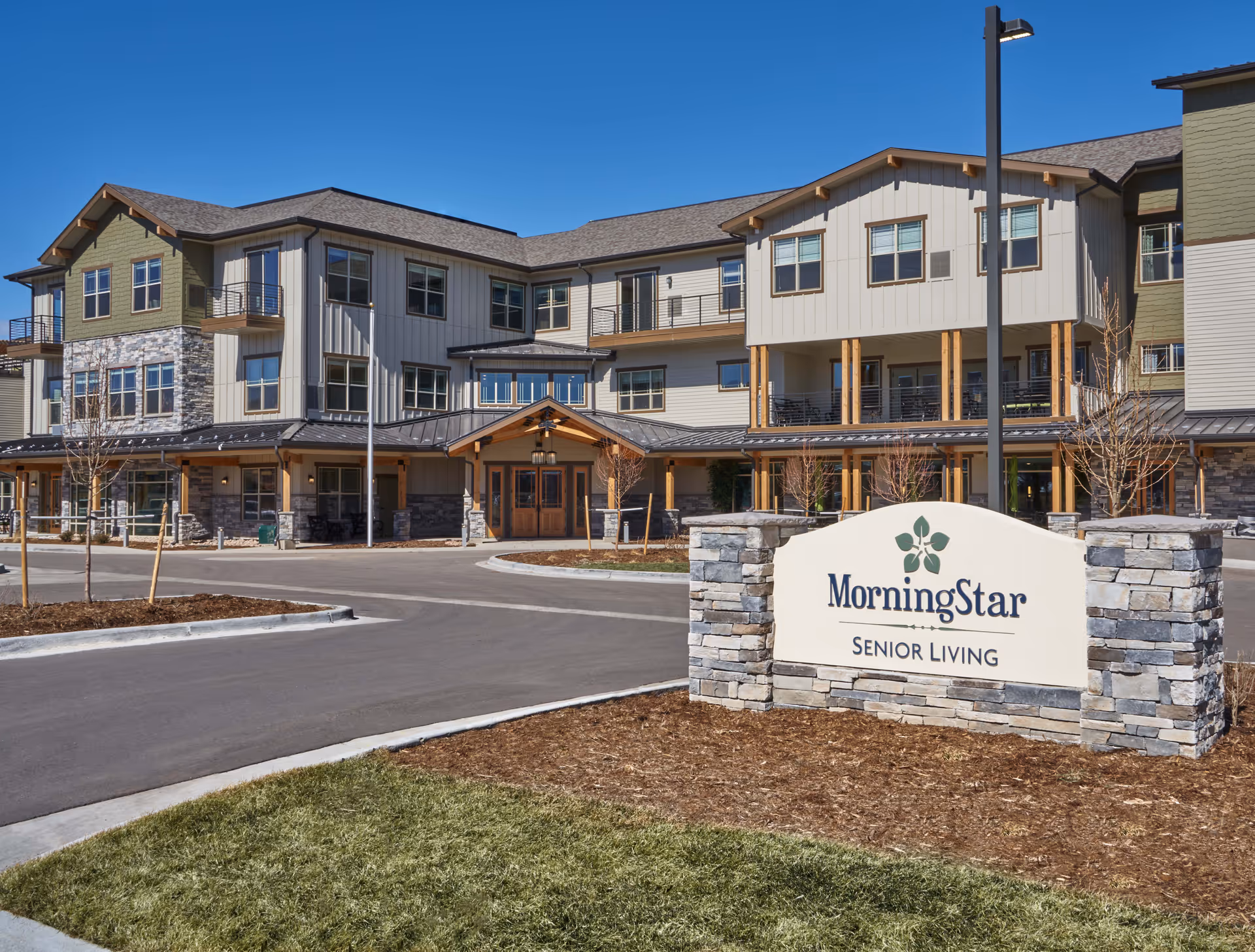 Front exterior of a three-story MorningStar Senior Living building with the main entrance, driveway, and a stone sign in the foreground.