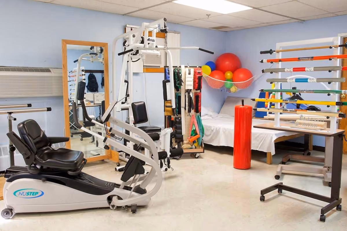 Rehabilitation gym with exercise machines, weights, and therapy balls in a blue-walled room.