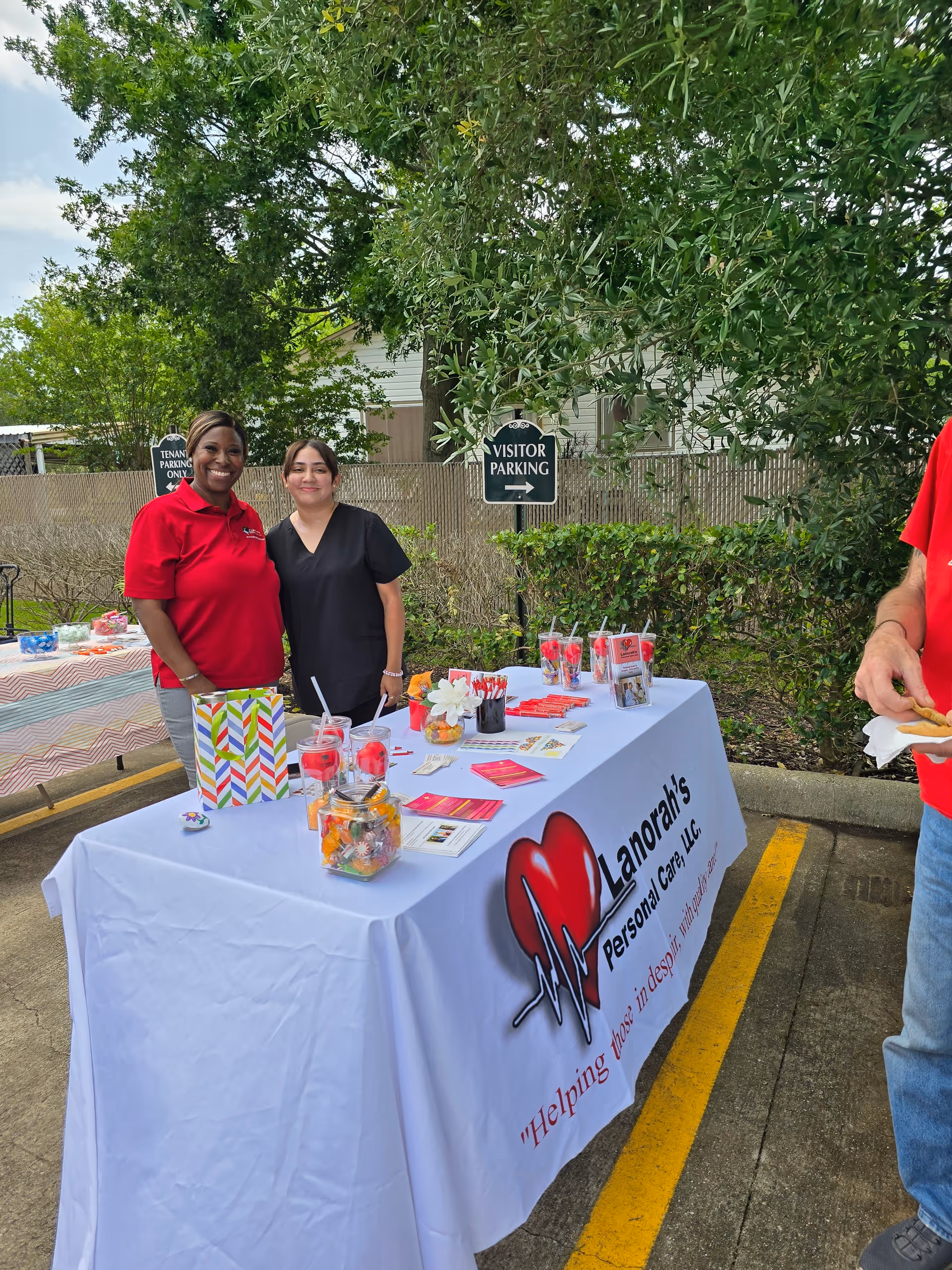 Two caregivers stand beside a promotional table outdoors at Lanorah's Personal Care.