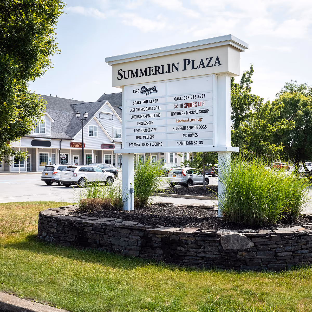 Large outdoor sign for Summerlin Plaza with storefronts, cars, and landscaped circular planter.