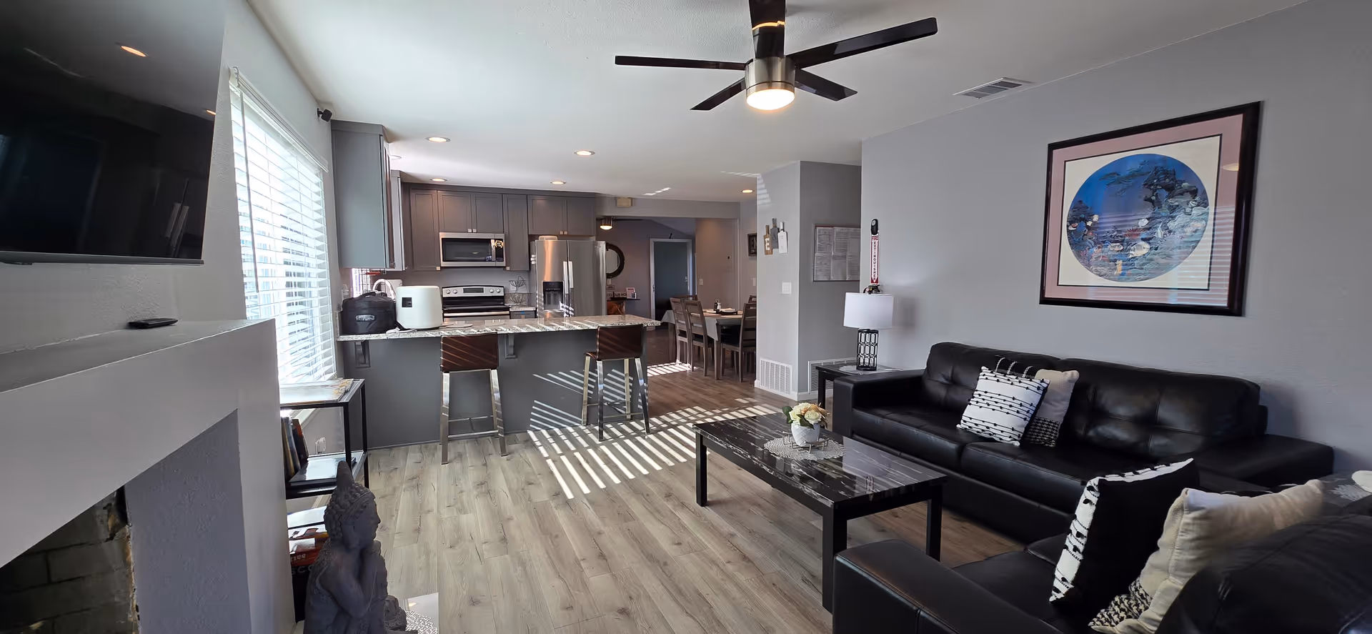 Open plan living area with a black leather sofa, coffee table, kitchen island, and large window.