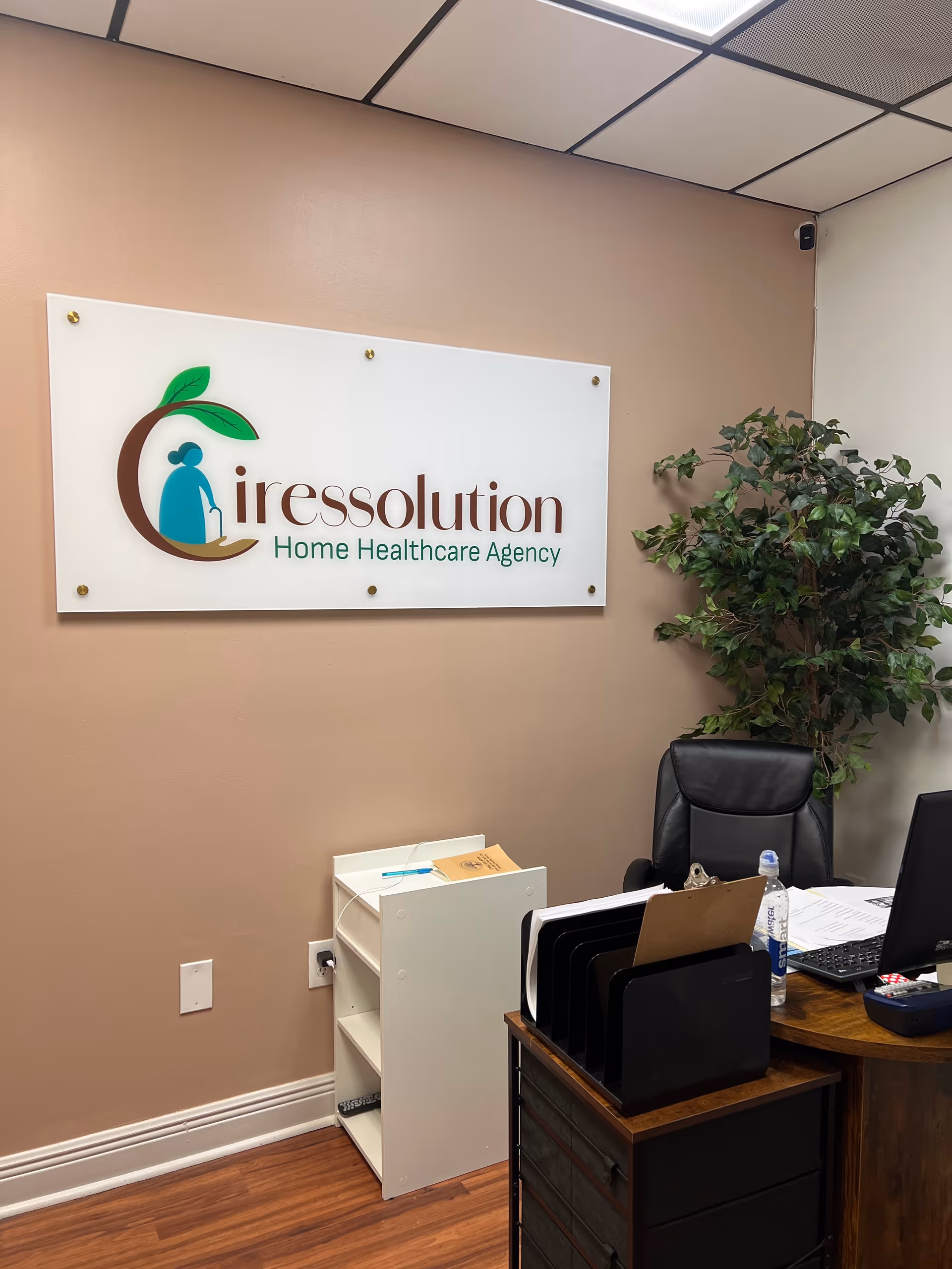 Office reception area with a wall sign reading Ciresolution Home Healthcare Agency and a plant.