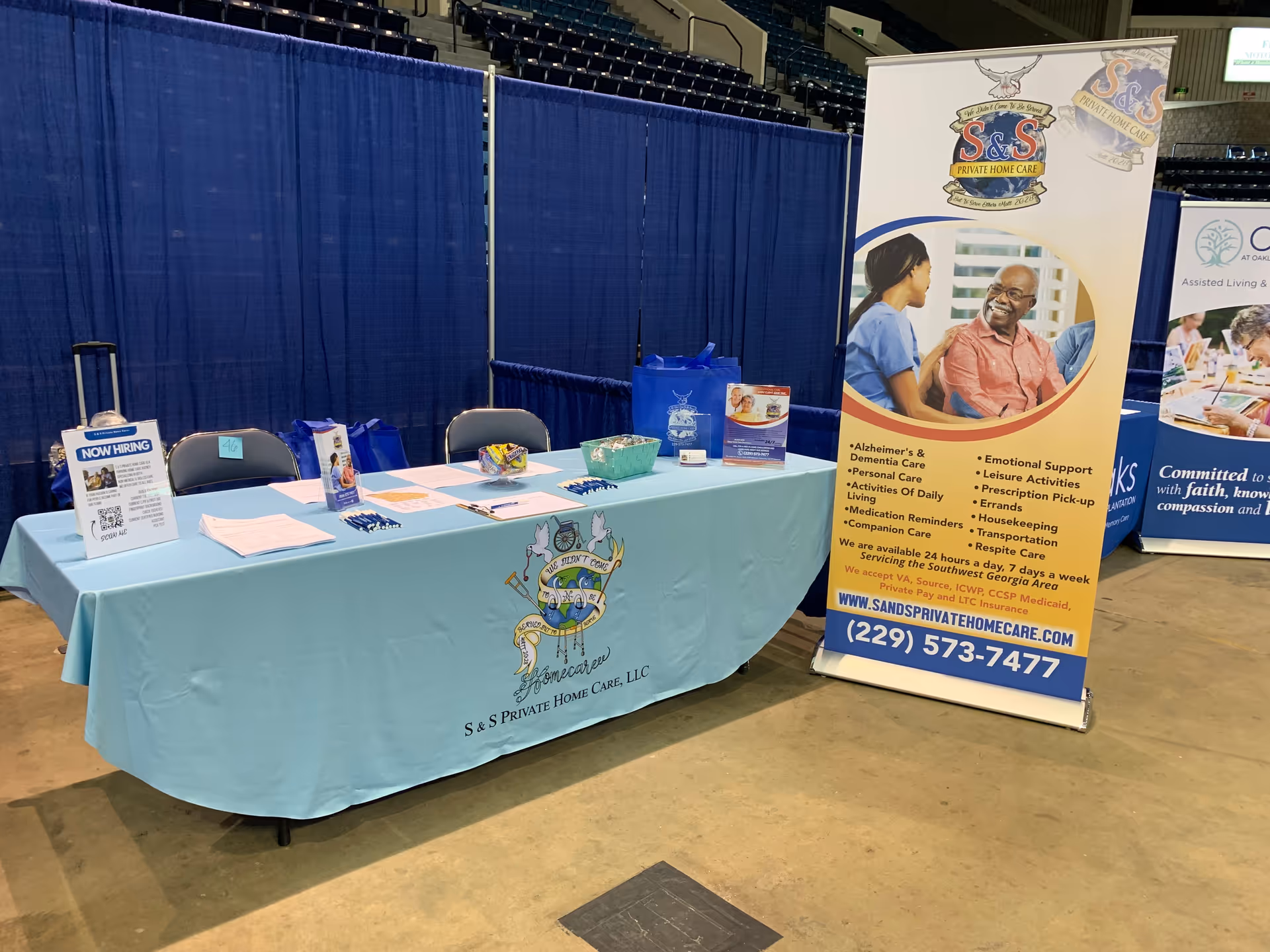 Exhibit table with teal cover, brochures, and a tall S&S Private Home Care banner indoors.