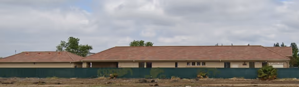 Single-story facility with brown-tiled roof, beige walls, and a green privacy fence.