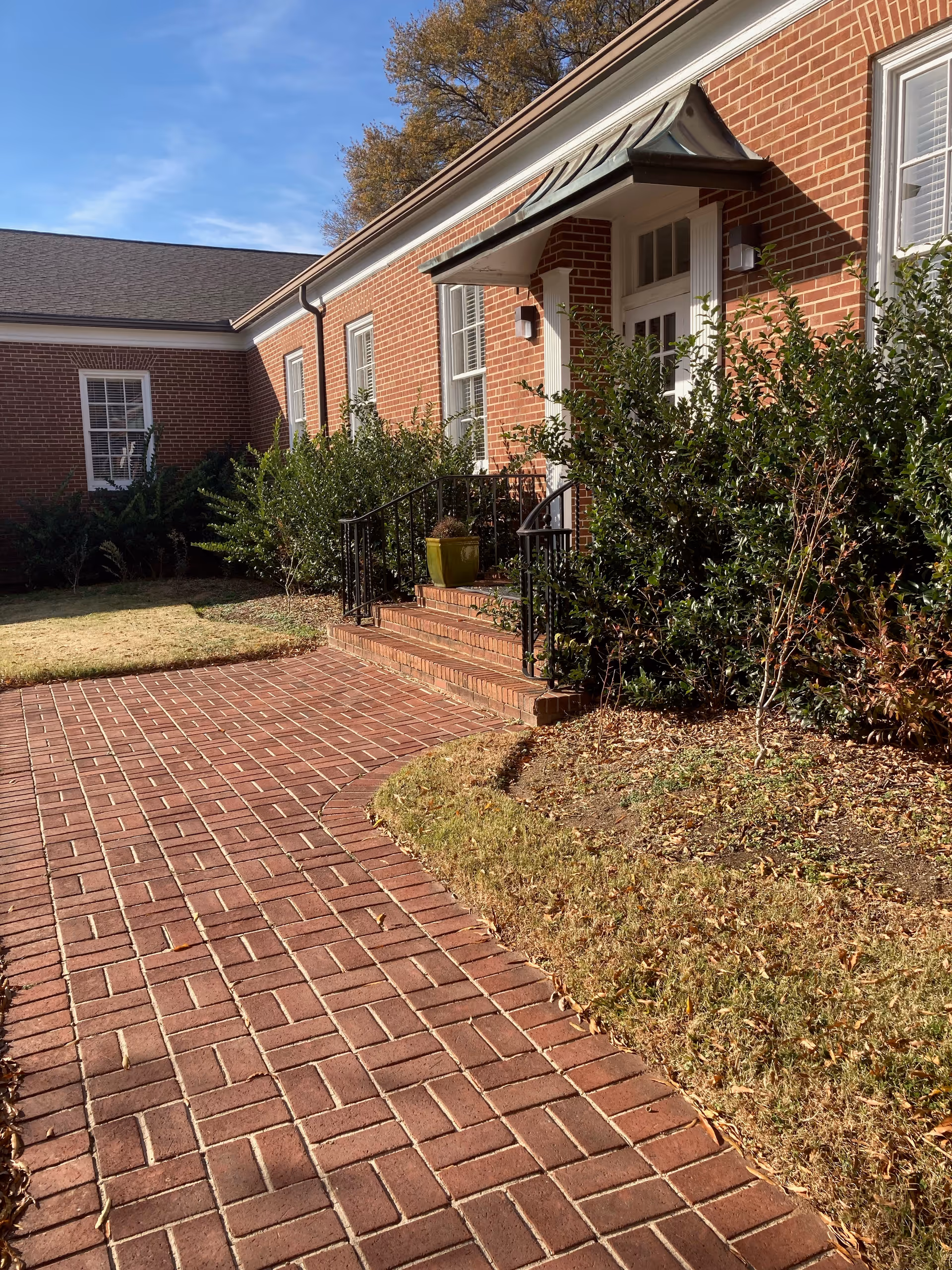 Brick building entrance with stairs, railing, and landscaped pathway.