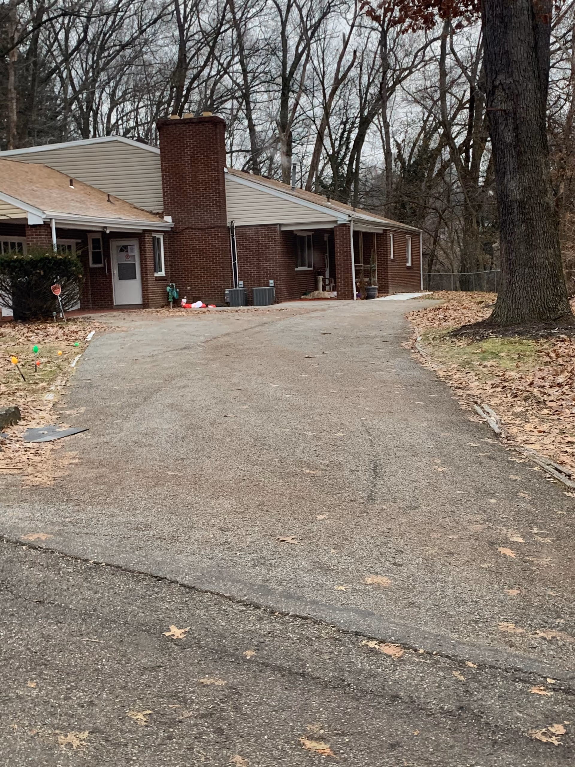 Brick, single-story care home with a driveway and leaf-covered grounds.