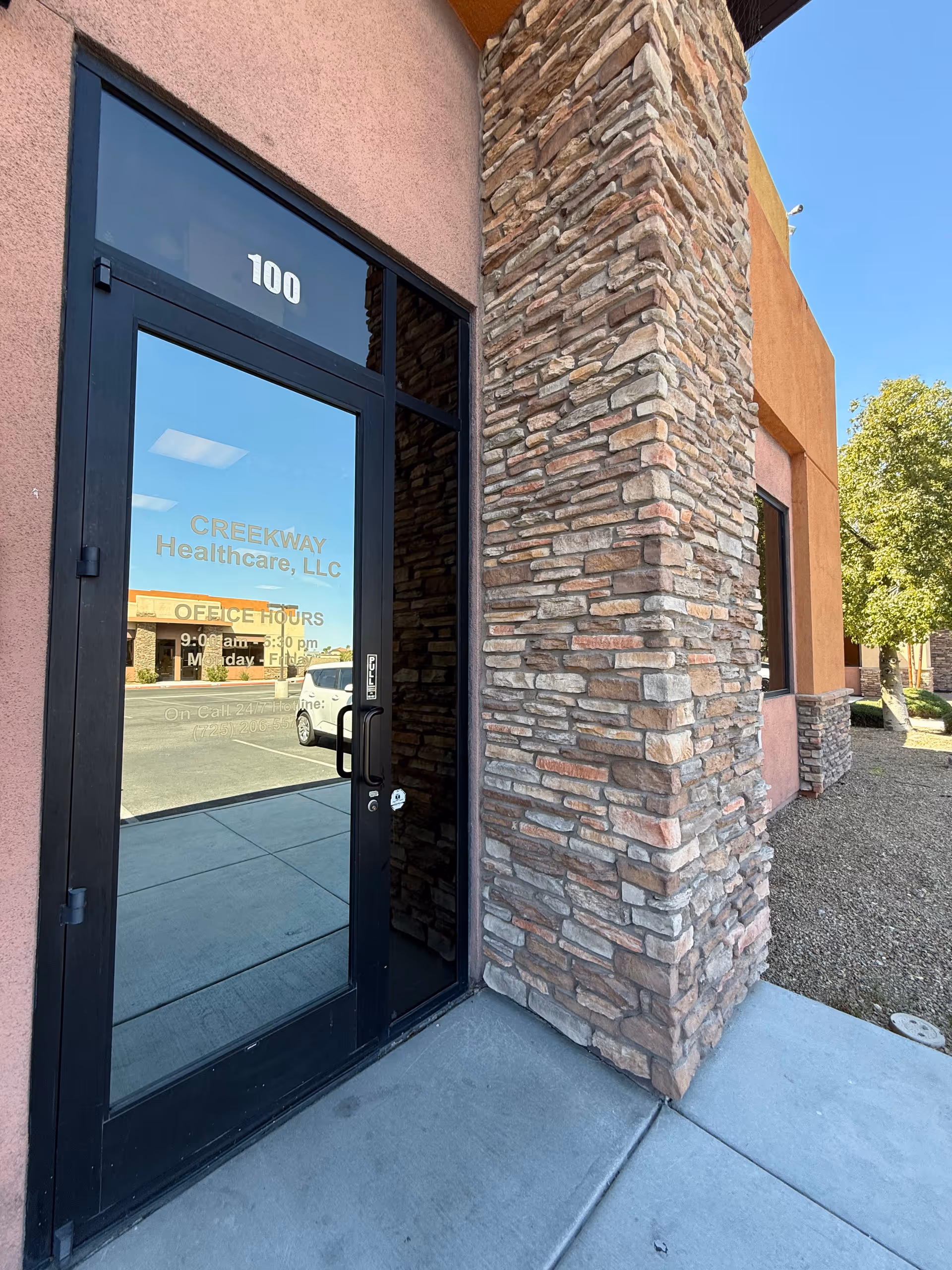 Exterior entrance of Creekway Healthcare with a glass door and stone column.