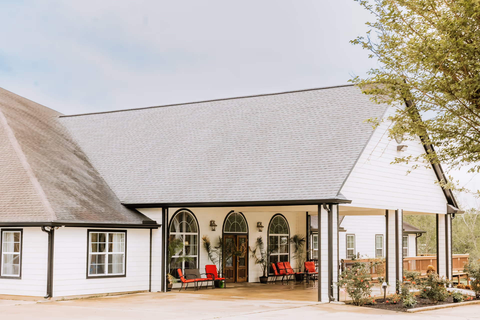 White building with arched front windows and red chairs under a covered entrance.