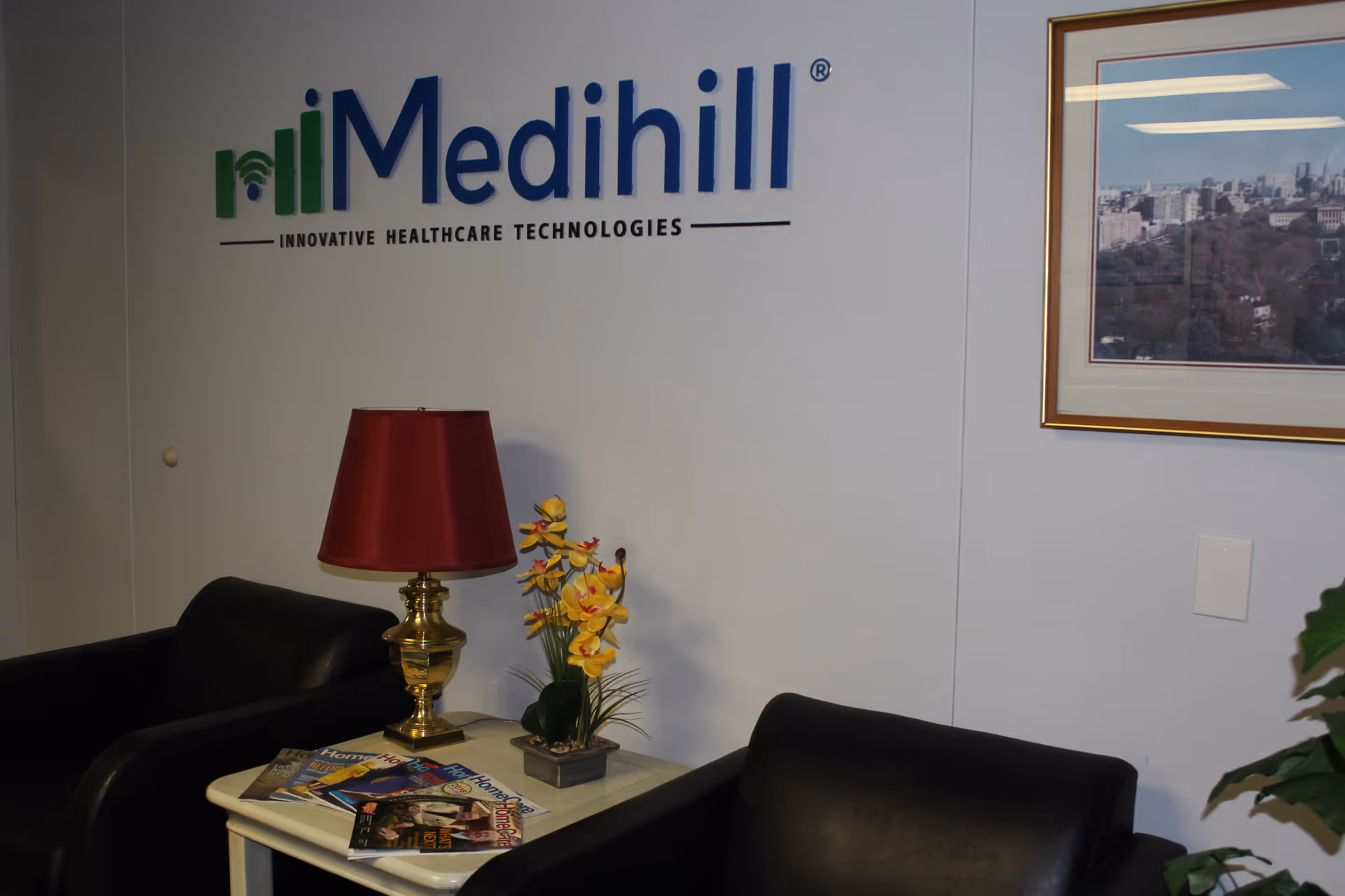 Interior lounge area with Medihill logo, black chairs, lamp, and magazines on a table.