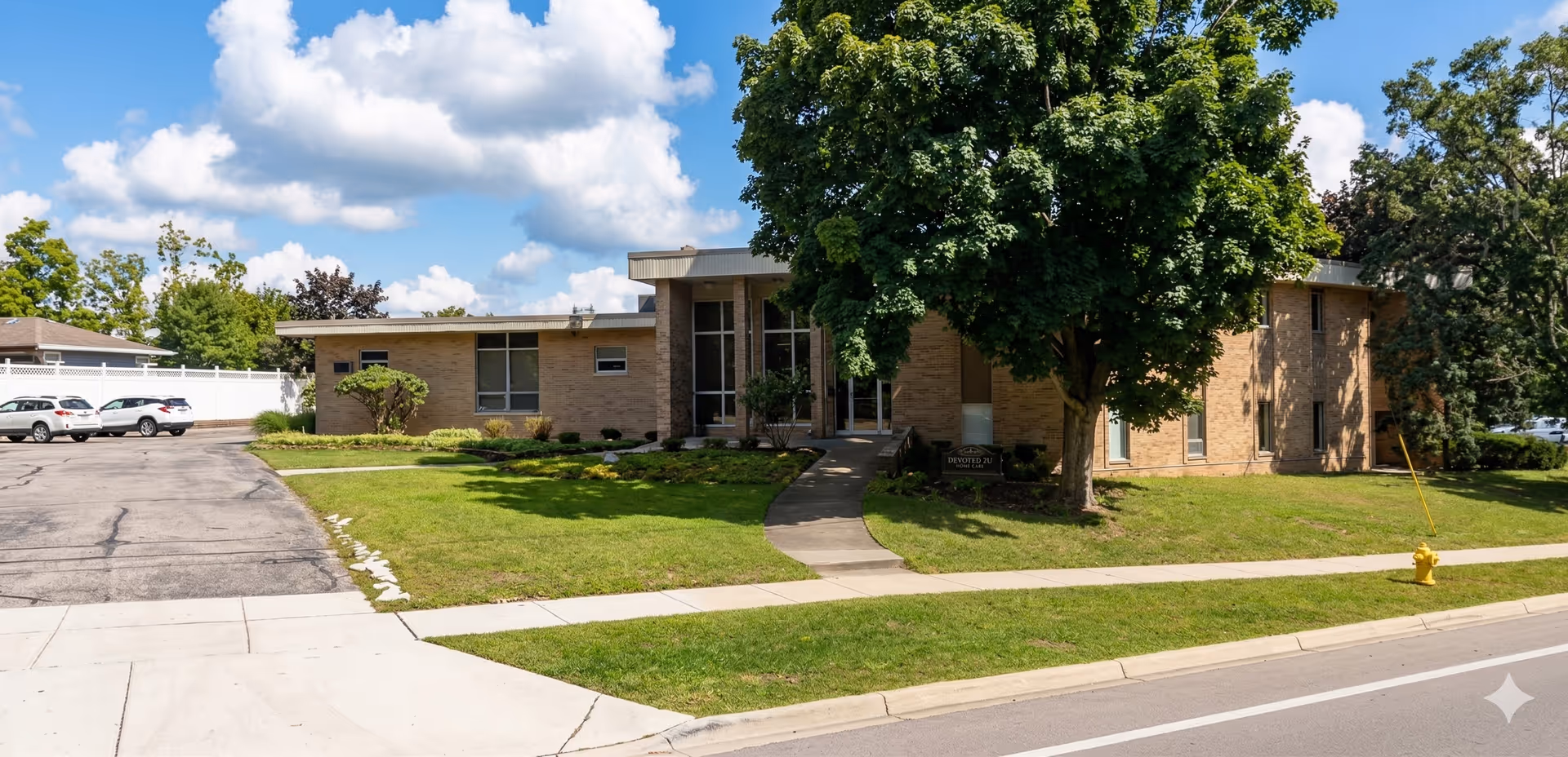 Front view of a brick senior care facility, with entrance, trees, and manicured lawn.